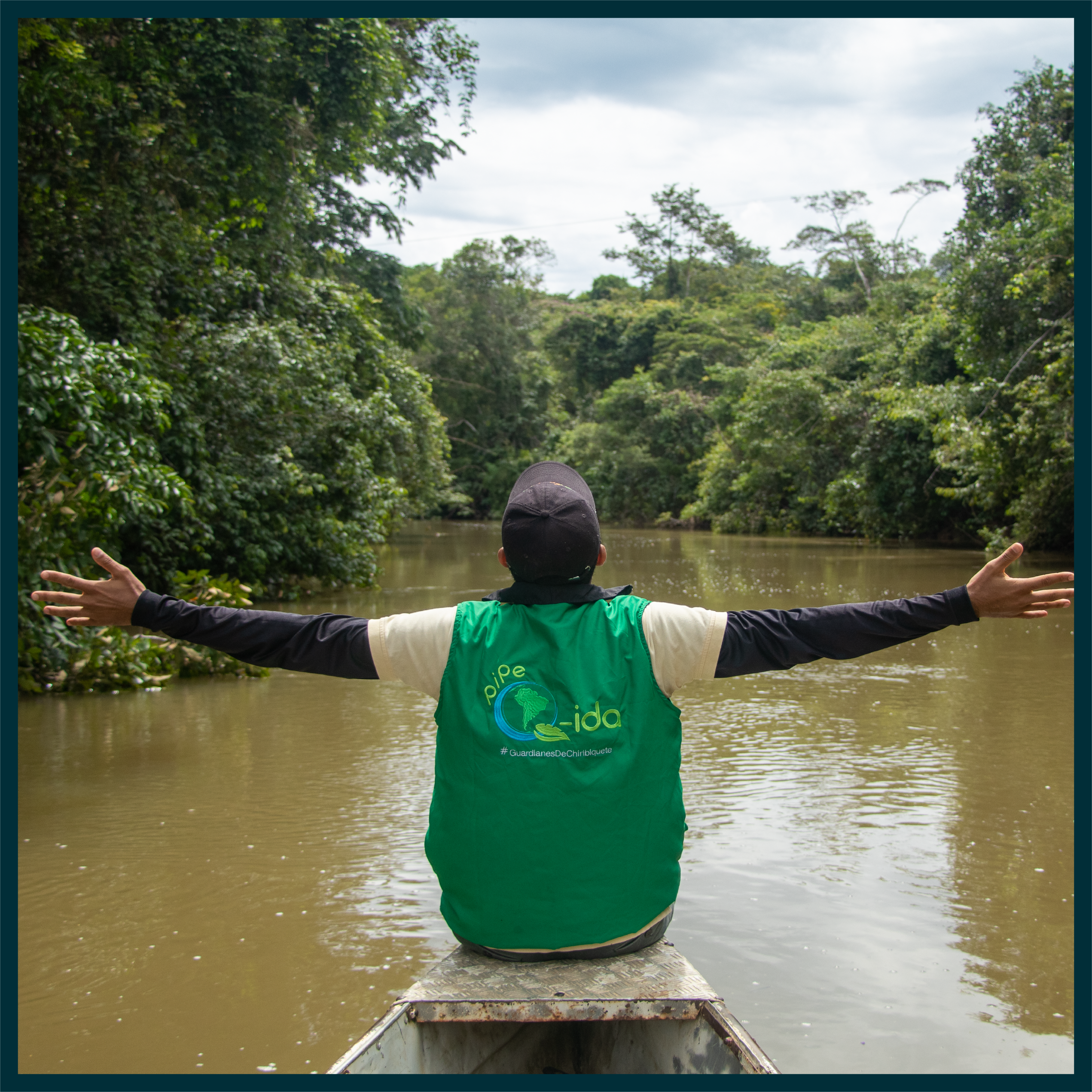 Image of Ambassador sat on the front of a long, wooden boat with arms outstretched, floating down a river in the jungle
