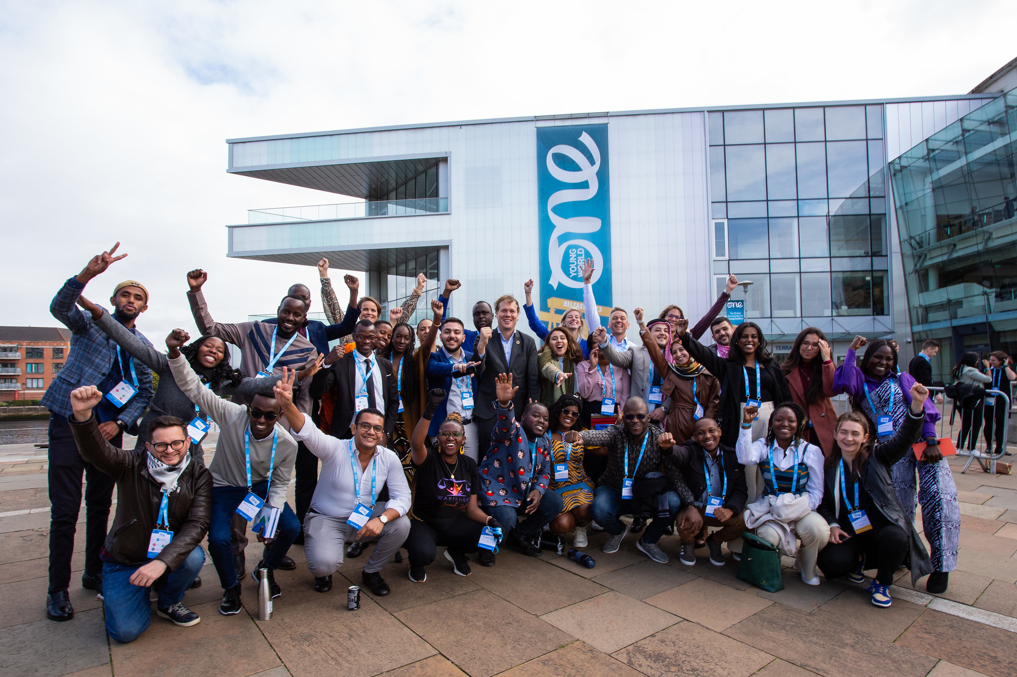 Group photo of One Young World attendees waving and smiling outside the Belfast International Convention Centre