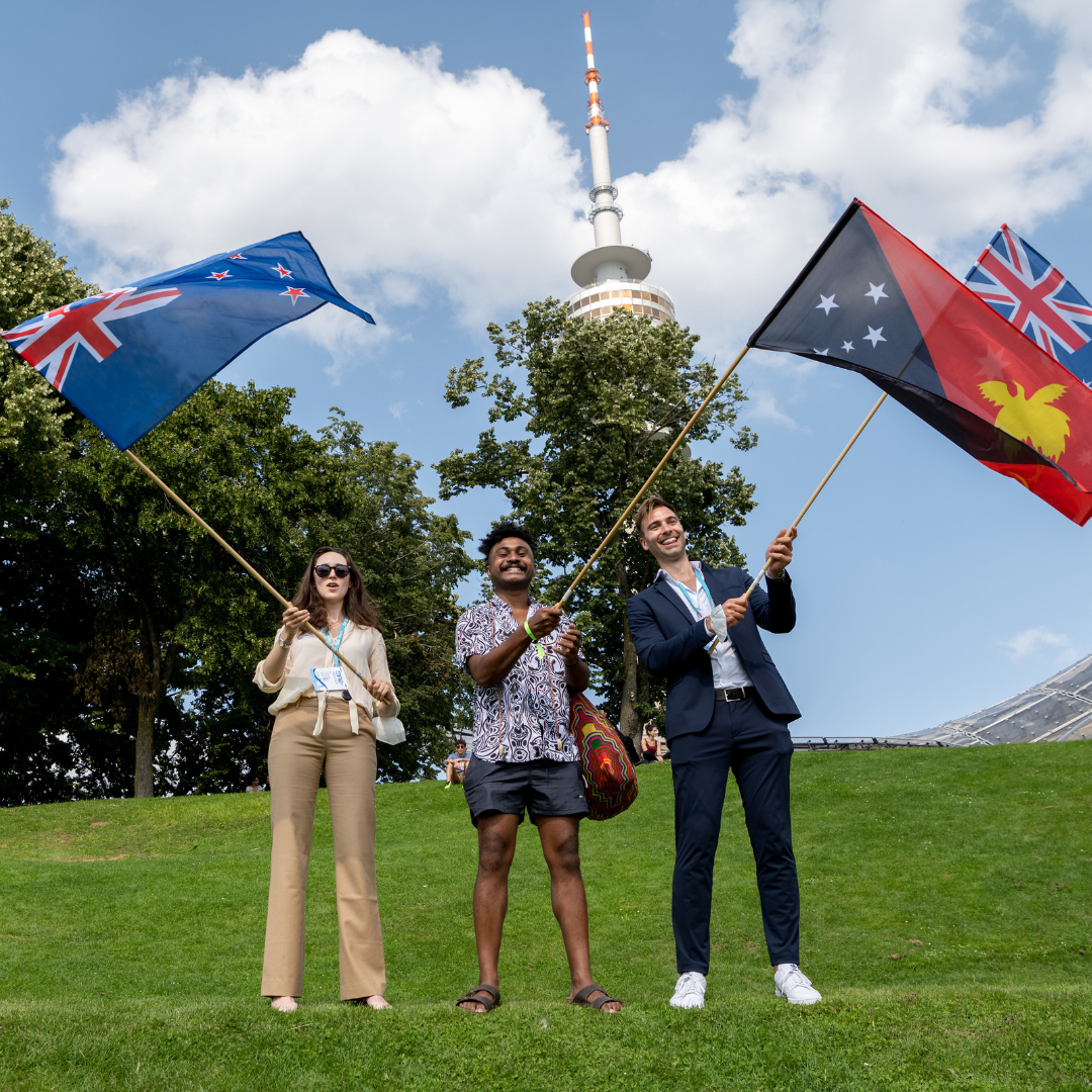 Three Delegates at One Young World smile into the camera waving their country's flag.