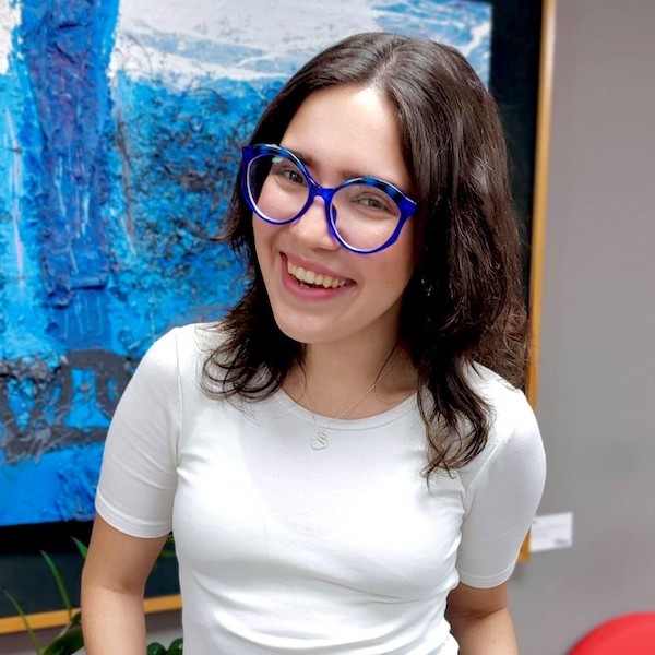 Camila Colmenares in white shirt, black trousers with blue painting in background