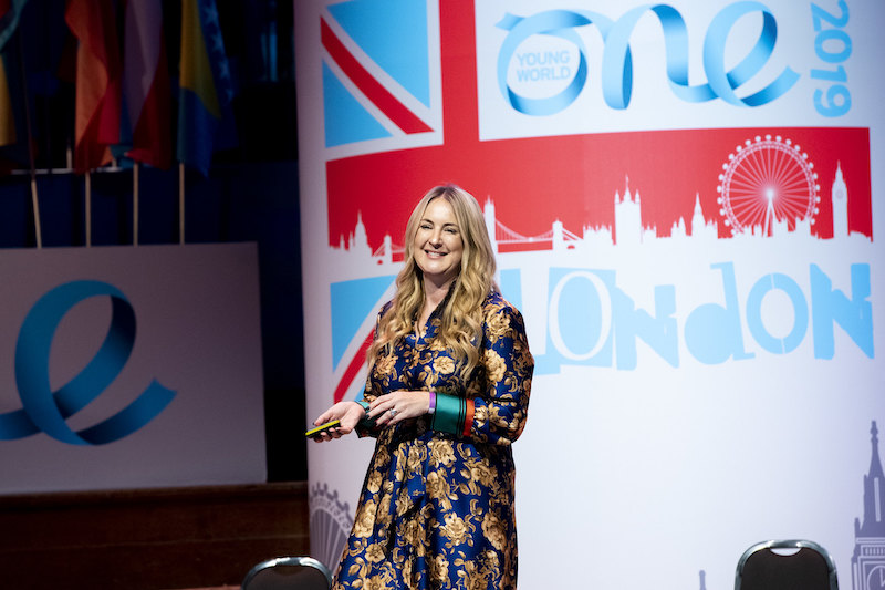 Sophie Howe wearing a royal blue with yellow-gold flowers outfit presenting at the OYW London Summit