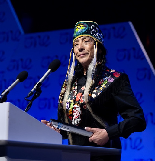 Speaker at the closing remarks for the Belfast 2023 One Young World Summit wearing traditional Indigenous garment and headress