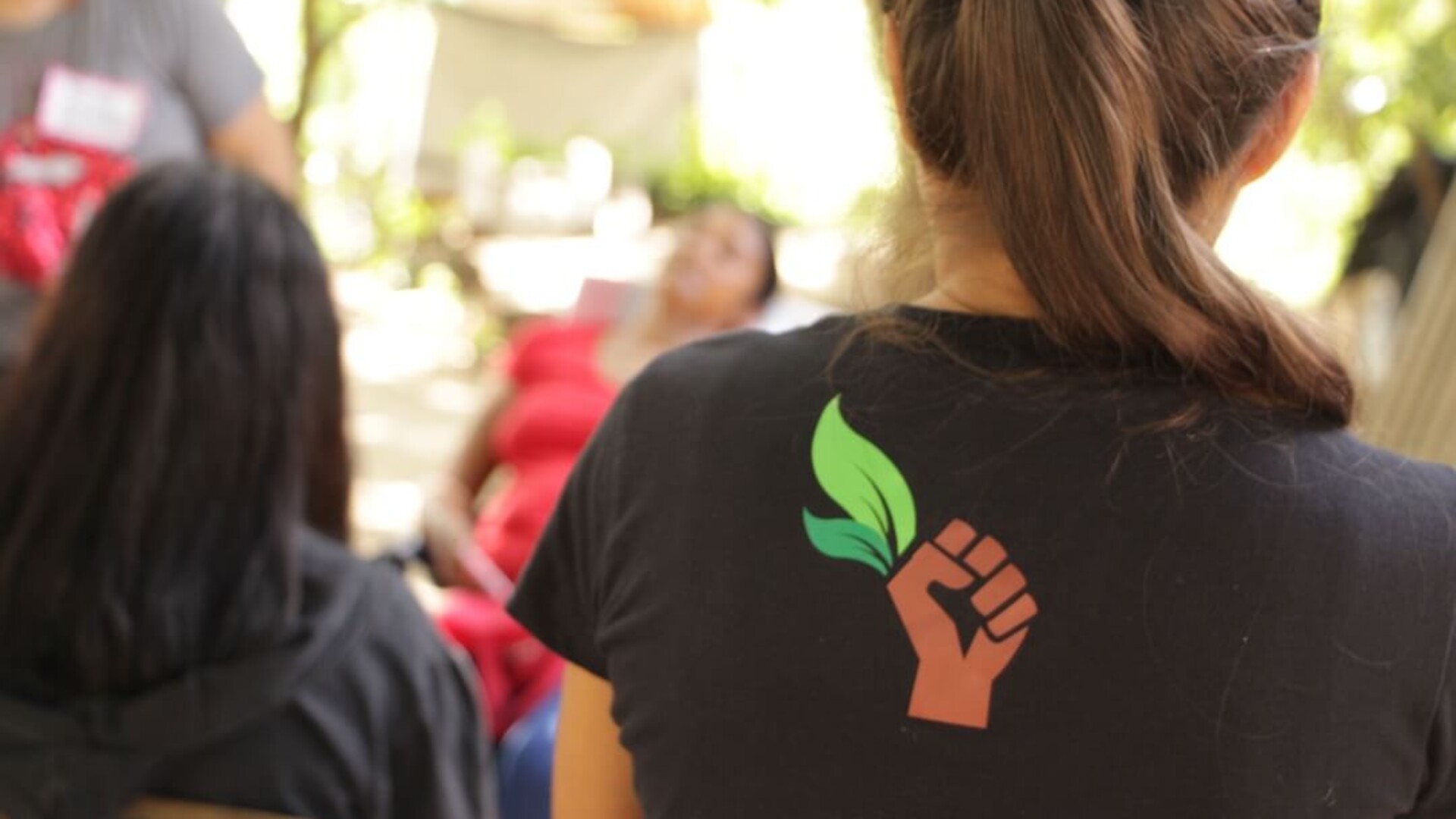 Woman facing away from camera wearing black tee-shirt with a graphic representing a fist clutching green leaves