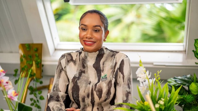Keithlin Caroo-Afrifa in pattern top sitting at desk surrounded by green indoor plants