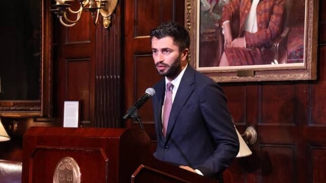 Rza Aliyev speaking at podium inside a baroque-style room