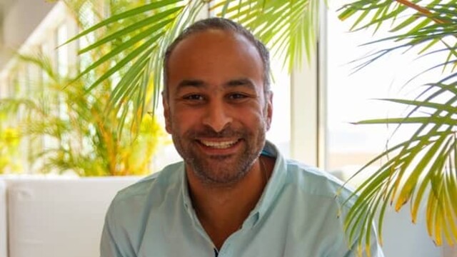 Seif Taher en chemise décontractée vert clair sur fond de canapé blanc et de plantes d'intérieur