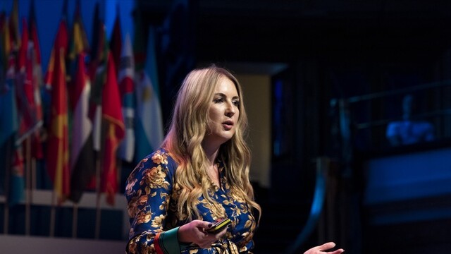 Sophie Howe wearing a royal blue with yellow-gold flowers outfit presenting at the OYW London Summit