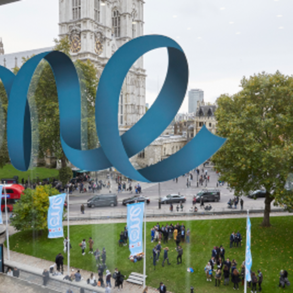 Large OYW ribbon logo on glass panel overlooking a landscaped green area and roadside with church in background