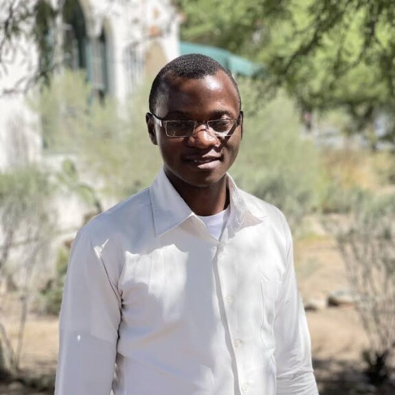 Harunah Damba with white shirt and glasses in sparse grassland background