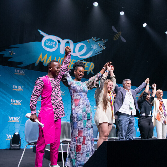 Peace ambassadors on stage at Manchester 22 summit wearing colourful outfits holding hands
