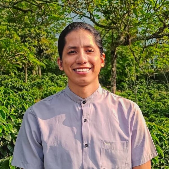 Johan Chavez en chemise blanche sur fond de buisson vert