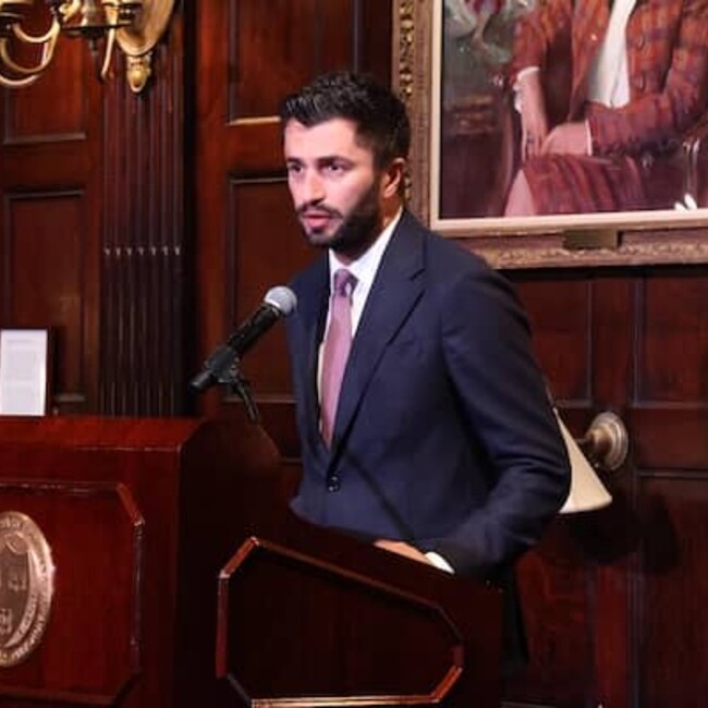 Rza Aliyev speaking at podium inside a baroque-style room