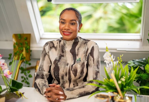 Keithlin Caroo-Afrifa in pattern top sitting at desk surrounded by green indoor plants