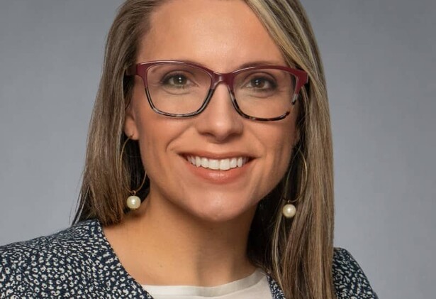 Portrait of Kayla Kelly in patterned white and grey suit and glasses against light grey background