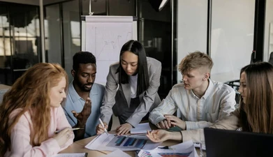 Smart-dressed staff around a table with notes and diagrams, discussing in a meeting environment