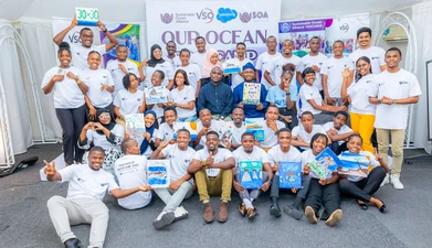 A group of approximately 30 people stands around a sign reading "our ocean" with marine-themed artwork. 