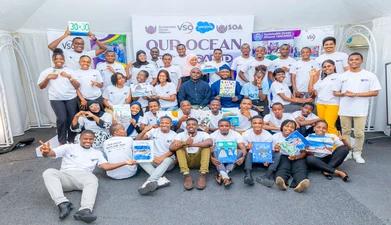 A group of approximately 30 people stands around a sign reading "our ocean" with marine-themed artwork. 