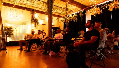 a group of people listen to a presentation under warm lighting