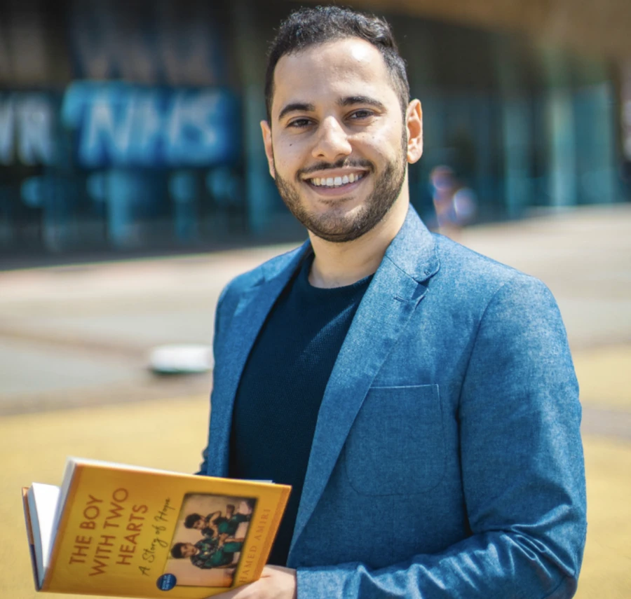 Hamed Amiri smiling holding his book The Boy with Two Hearts.