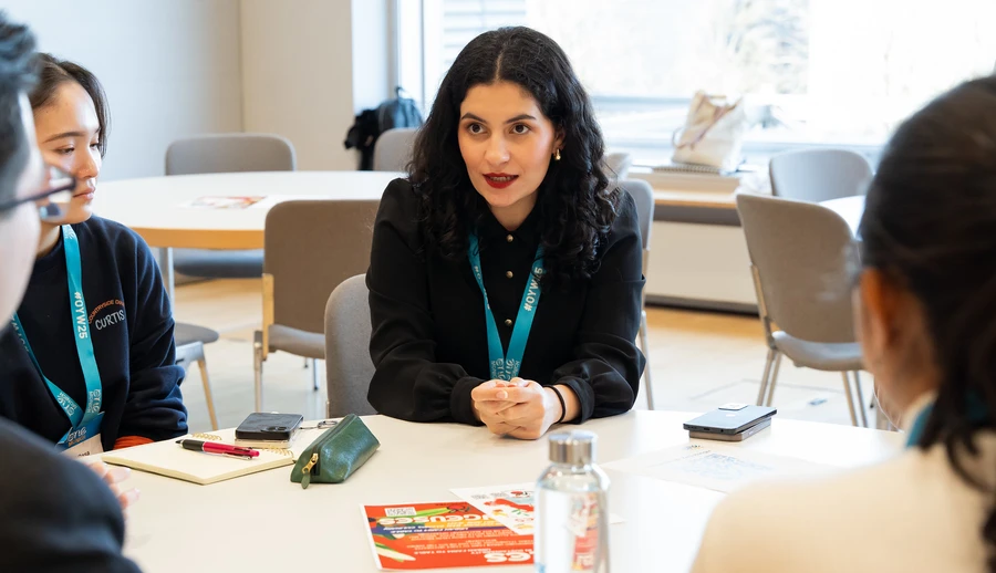 woman with black top and black hair sitting at a table with other people discussing