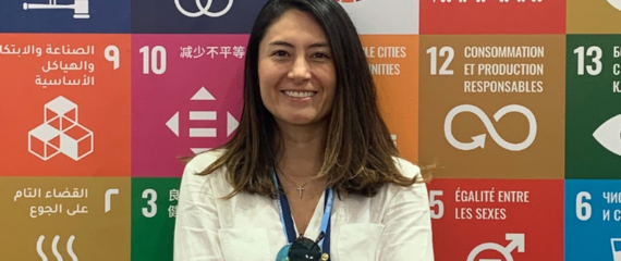 Picture of Alejandra Tellez smiling in front of a step and repeat showing the 17 Sustainable Development Goals