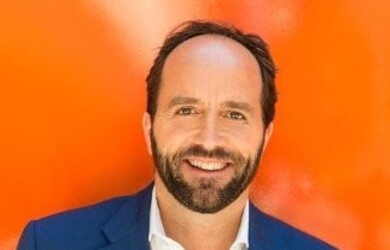 David portrait wearing white shirt and navy blue blazer against orange background