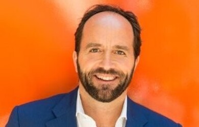 David portrait wearing white shirt and navy blue blazer against orange background