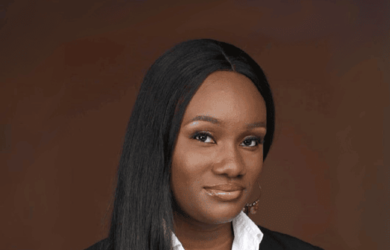 Debbie portrait, wearing white formal shirt and black blazer against brown background