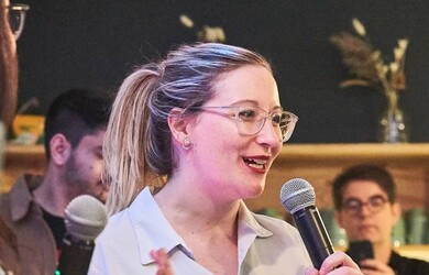 Florence portrait, wearing white formal shirt, holding microphone, speaking publicly at an event