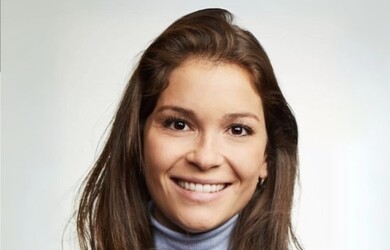 Laura portrait wearing light blue turtleneck sweater and black blazer against white grey background