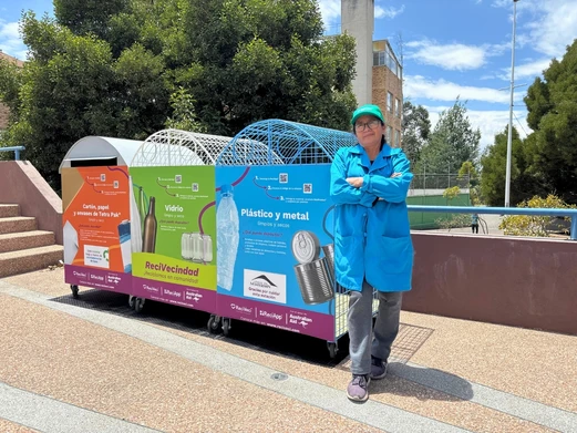 a waste collector poses in front of sorting bins