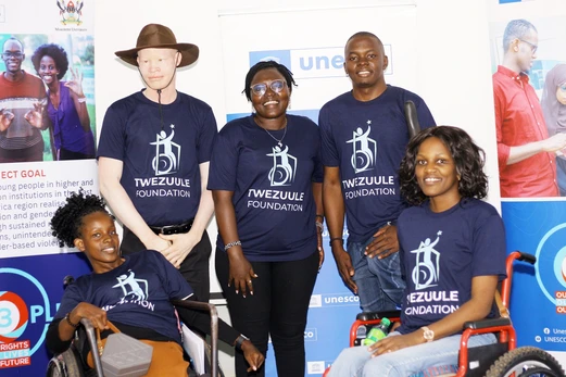 A group of Ugandan people with disabilities stands in front of a UNESCO sign