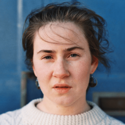 Portrait of Grug Muse in white jumper against blue background