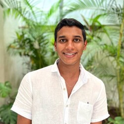 Portrait of Joshua Aguilar Valdés in white short-sleeved shirt against background of indoor plants