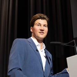 David Habluetzel in formal attire speaking on stage