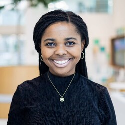 Maphrida Wehrli portrait wearing black turtleneck top and necklace against blurred indoor room background