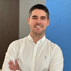 Portrait of Mark Heasman wearing All-Saints smart white shirt against brown, grey and blue background